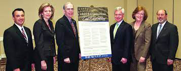 Six people stand around a printed pledge on an easel in a conference room. Individuals are not identified in this photograph.